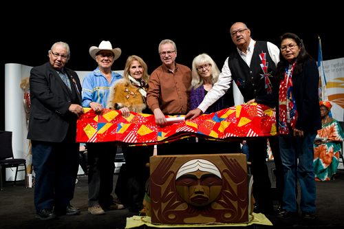 Un groupe de personnes, dont le juge Murray Sinclair, tend une courtepointe au-dessus de la boîte en bois cintré.