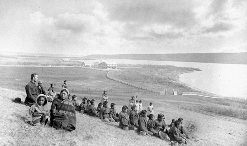 Des élèves autochtones et des membres du personnel religieux sont assis sur une colline surplombant une rivière près du pensionnat autochtone de Qu’Appelle, en Saskatchewan.