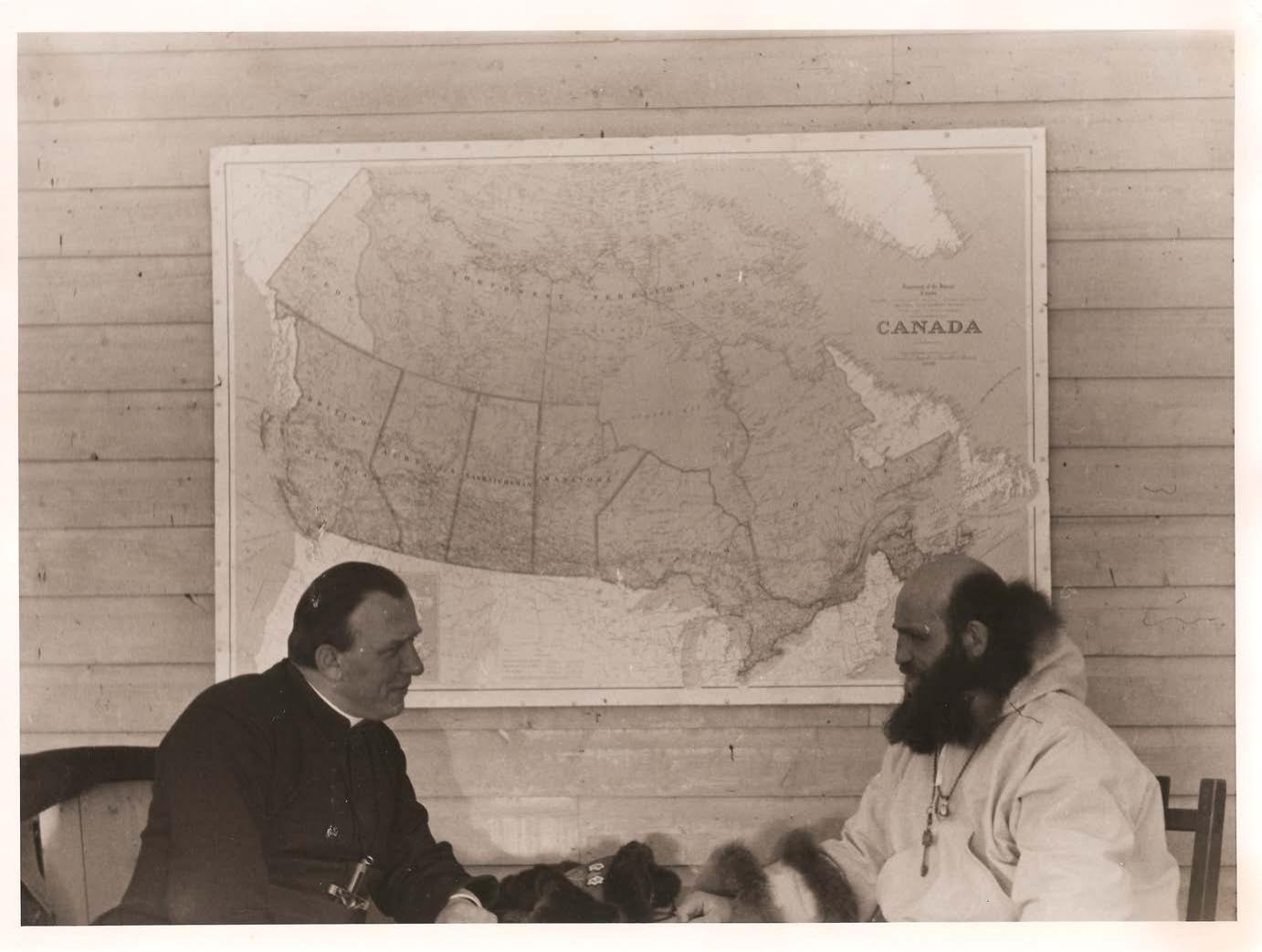 Father Schulte and Father Henri Belleau sit in front of a map of Canada.
