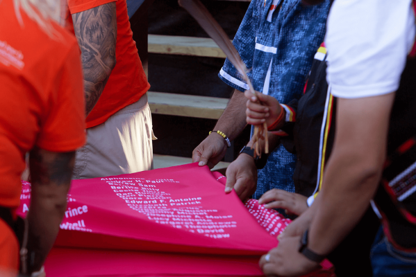Gros plan de quatre personnes pliant le tissu commémoratif et une personne tenant une plume d’aigle par-dessus le tissu