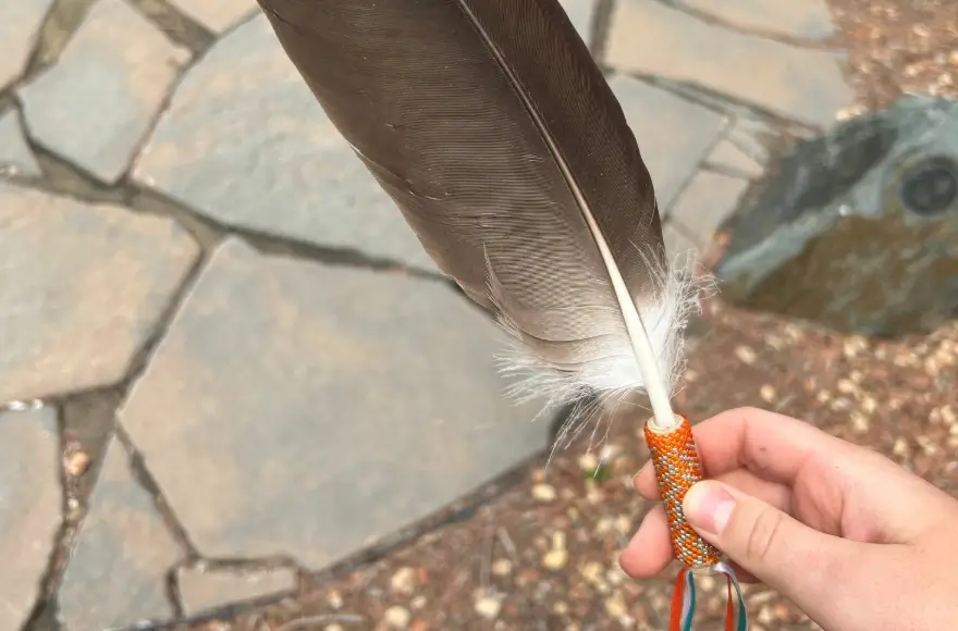 A person holding an eagle feather with a decorative beaded handle.