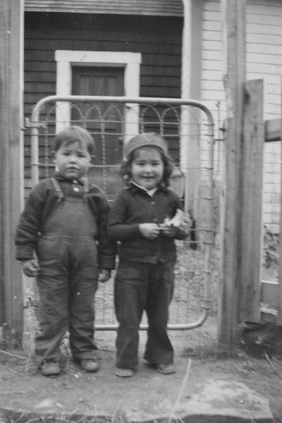 Black and white photo of Indigenous children and an adult woman in winter clothing, standing in a snowy landscape.