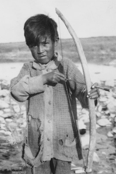 Black and white photo of an Indigenous boy holding a bow and arrow.