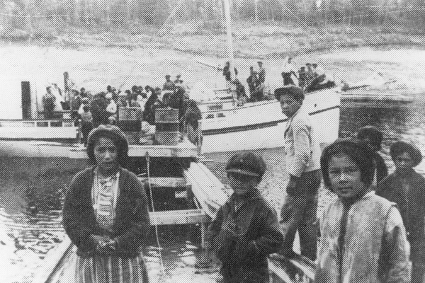 Black and white photo of Indigenous children standing on a dock near a crowded boat.